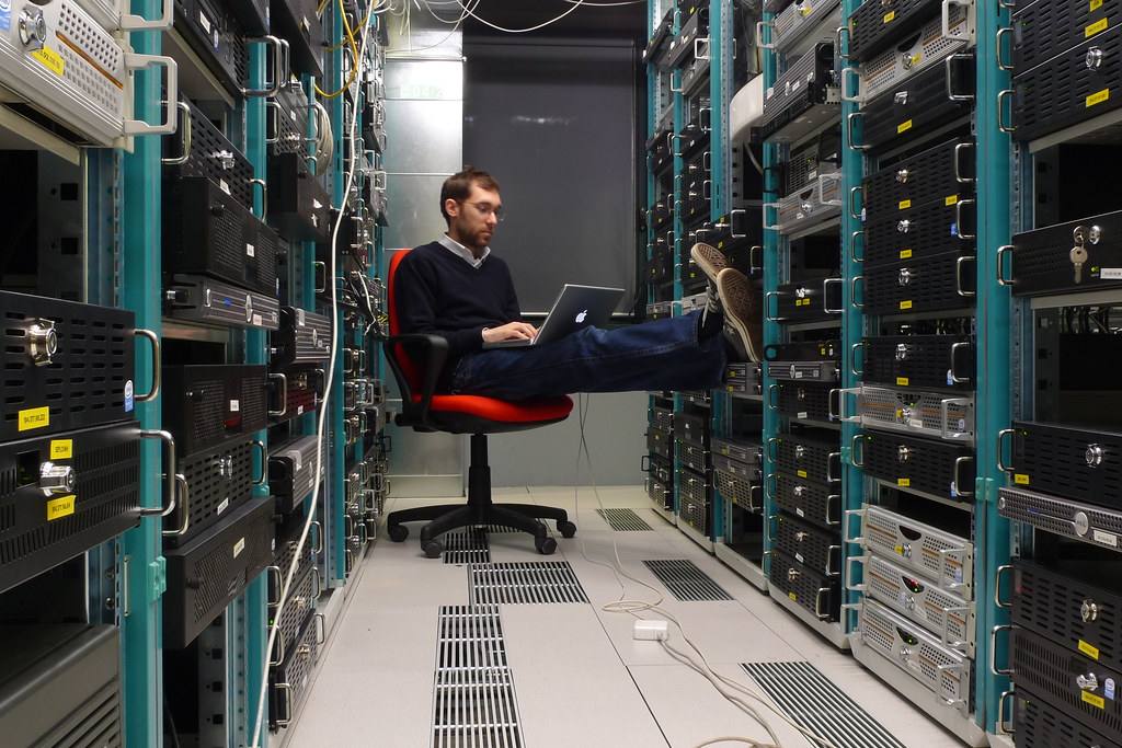Technik s notebookem sedí mezi dvěma řadami serverových skříní