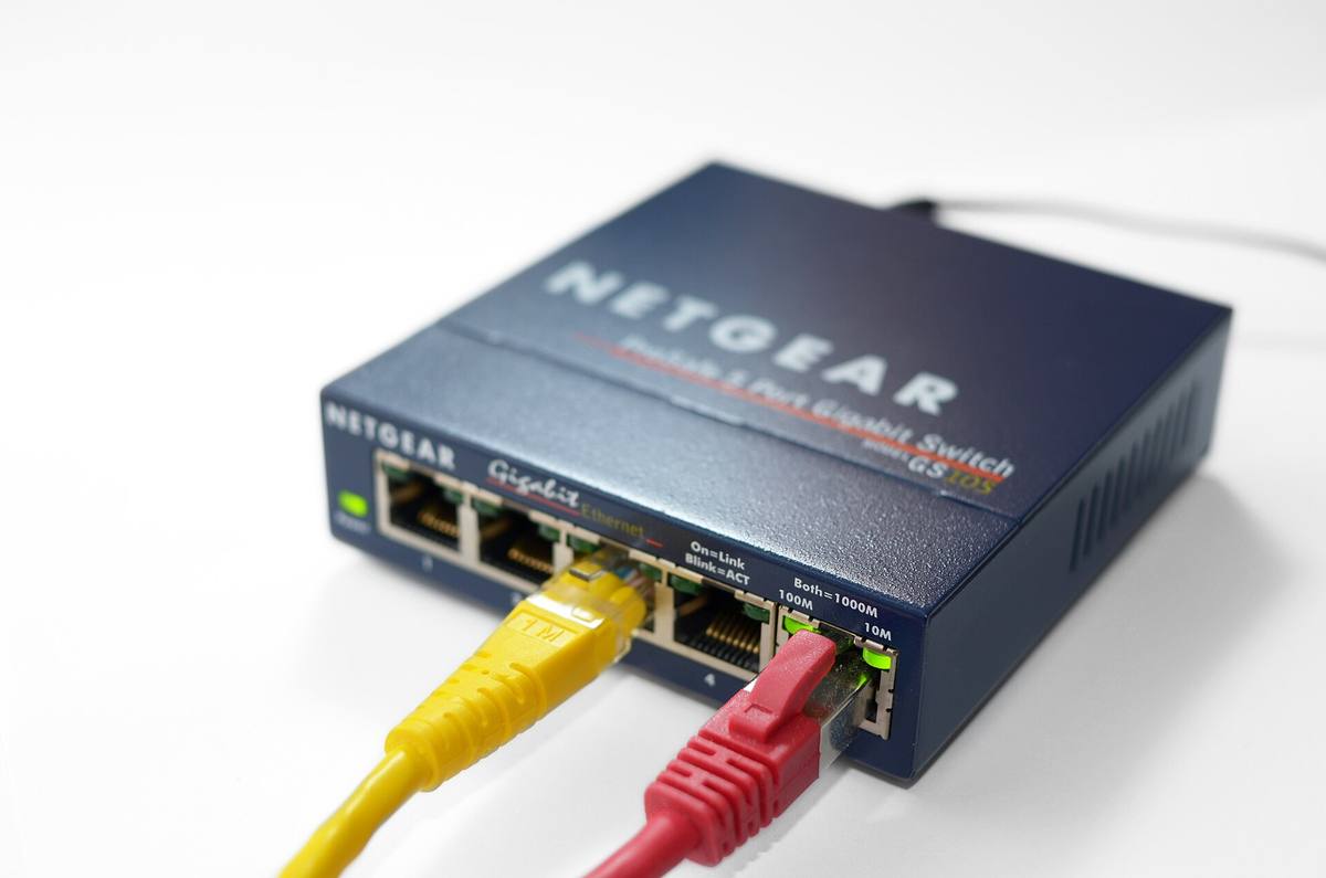 Pětiportový gigabitový přepínač Netgear s jedním zapojeným červeným a jedním nezapojeným žlutým kabelem